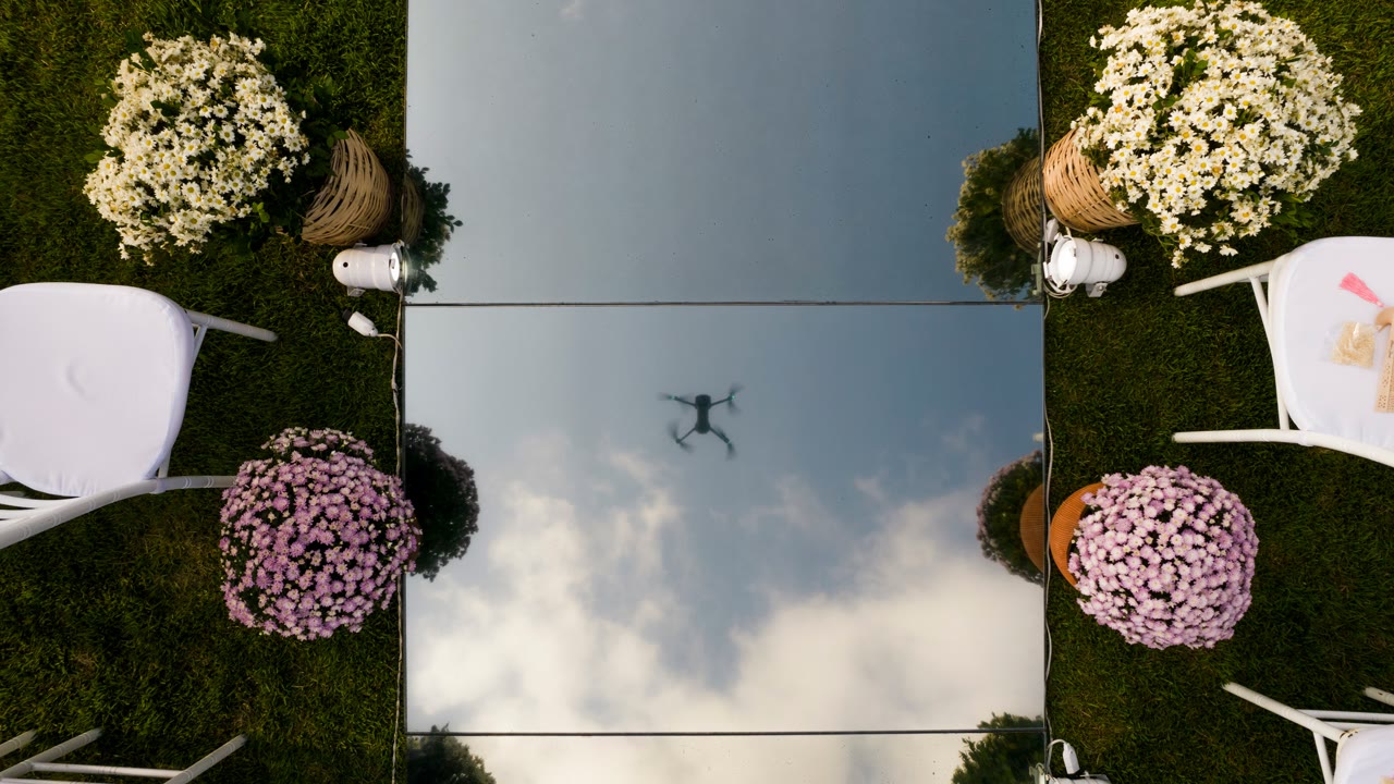 Top-down aerial drone shot of a wedding ceremony setup, the drone reflected in a mirror floor